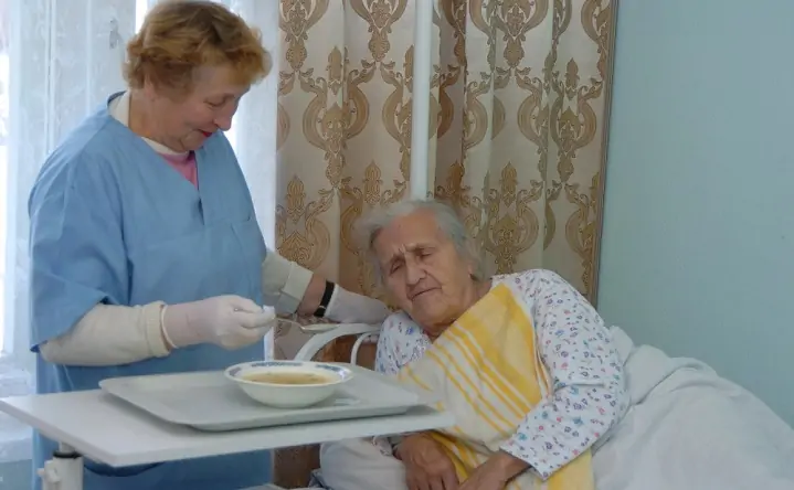 Соцработник кормит пожилую женщину. Фото Vademec.ru